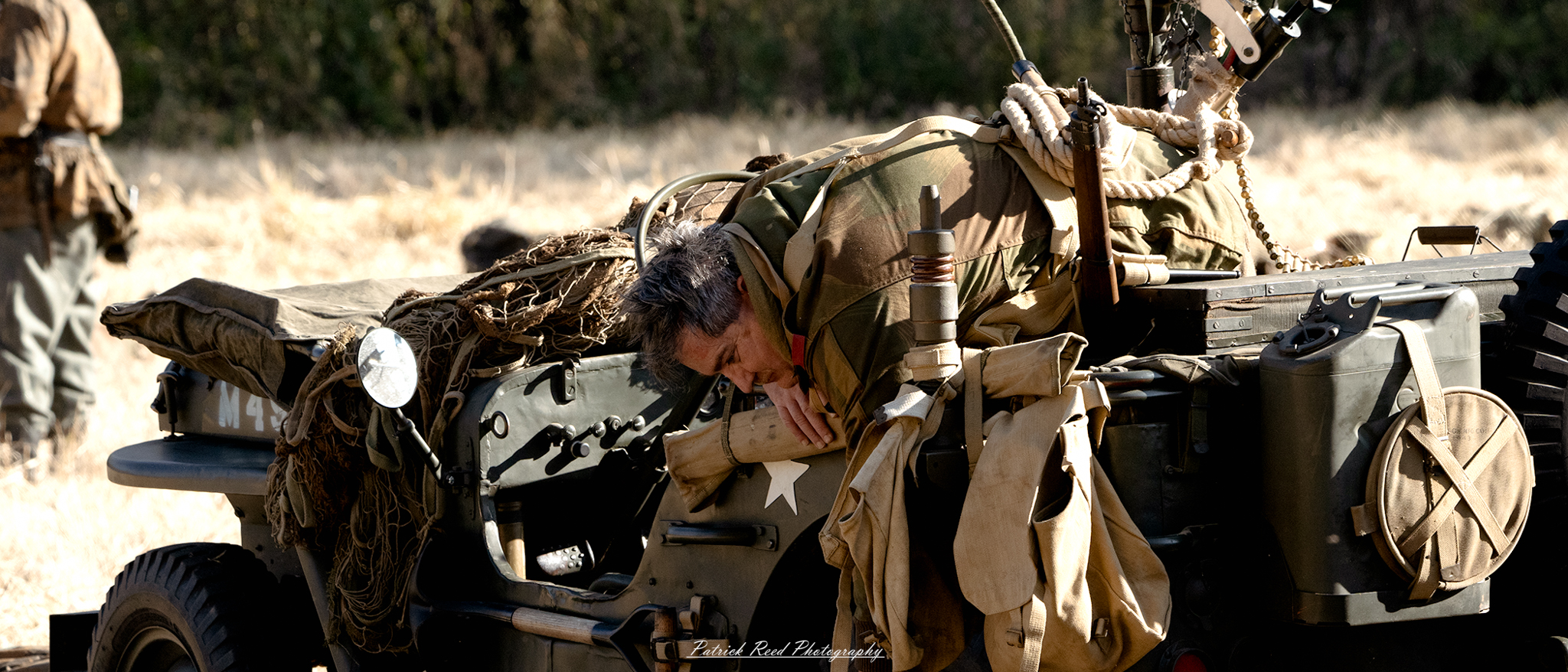 "A fallen WWII jeep driver, slumped over the wheel of the vehicle after a fierce battle. The jeep is damaged, surrounded by debris, with the driver’s uniform bloodied and torn. The scene is solemn, capturing the harsh realities and loss of war, set against a war-torn battlefield."